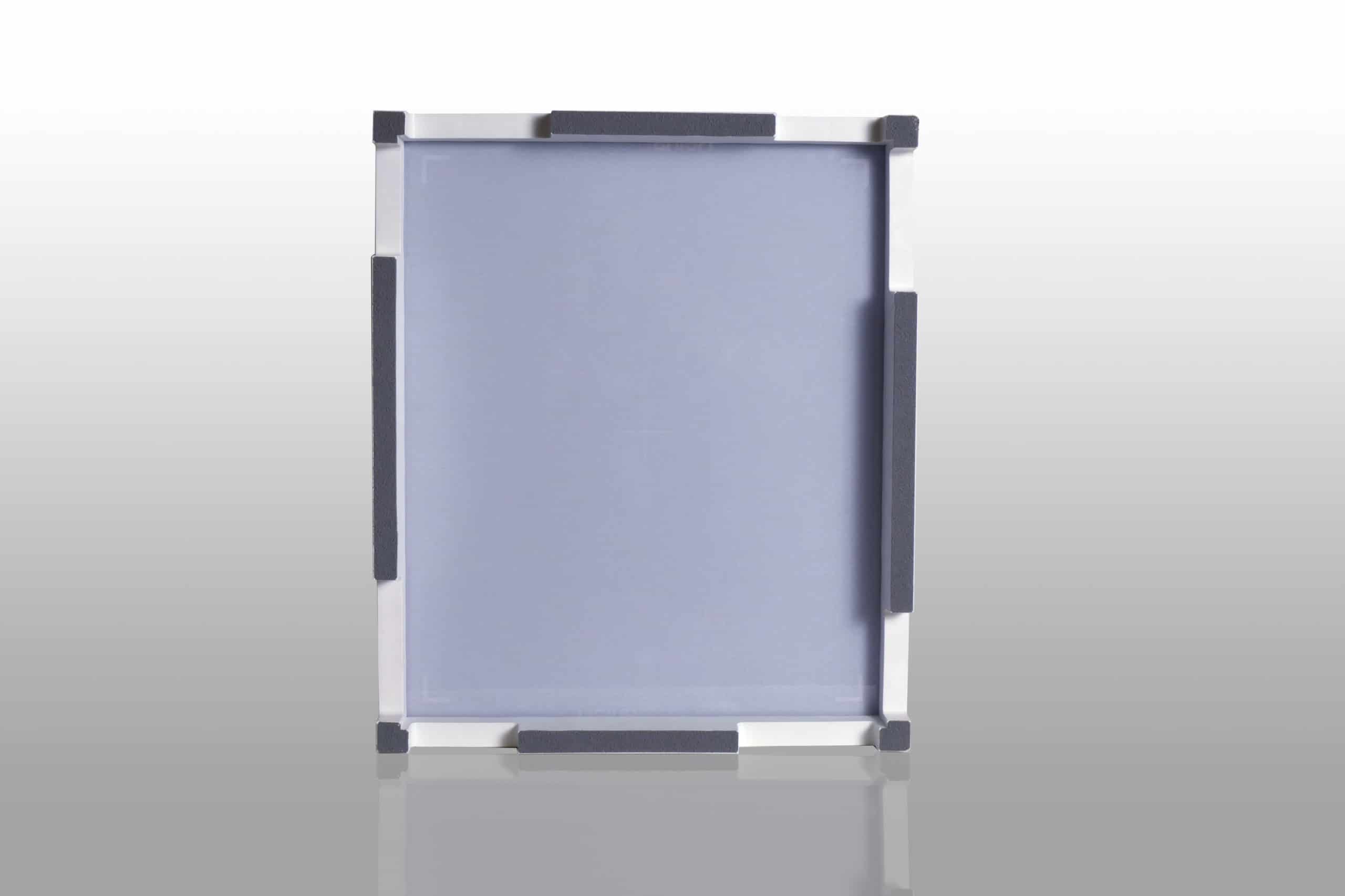Square gray panel with white frame and dark protective pads on all sides, placed on a reflective surface.