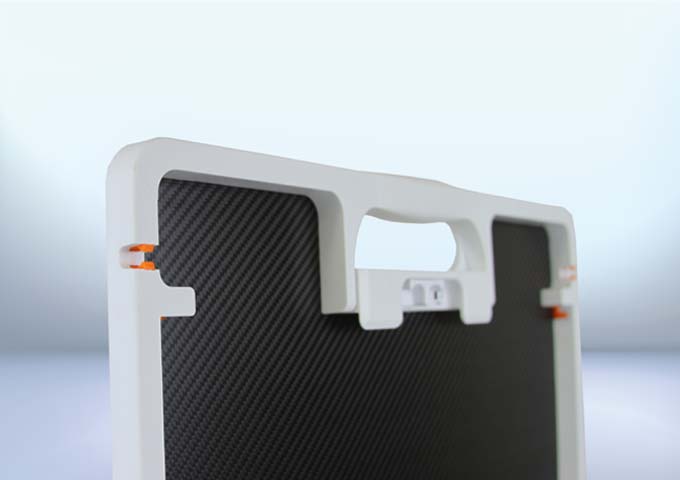 Close-up of a grid with a white frame, black surface, top handle, and orange side clips