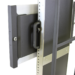 Close-up of a black mounting bracket with a sturdy handle attached to a metallic vertical frame featuring evenly spaced holes and support bars.